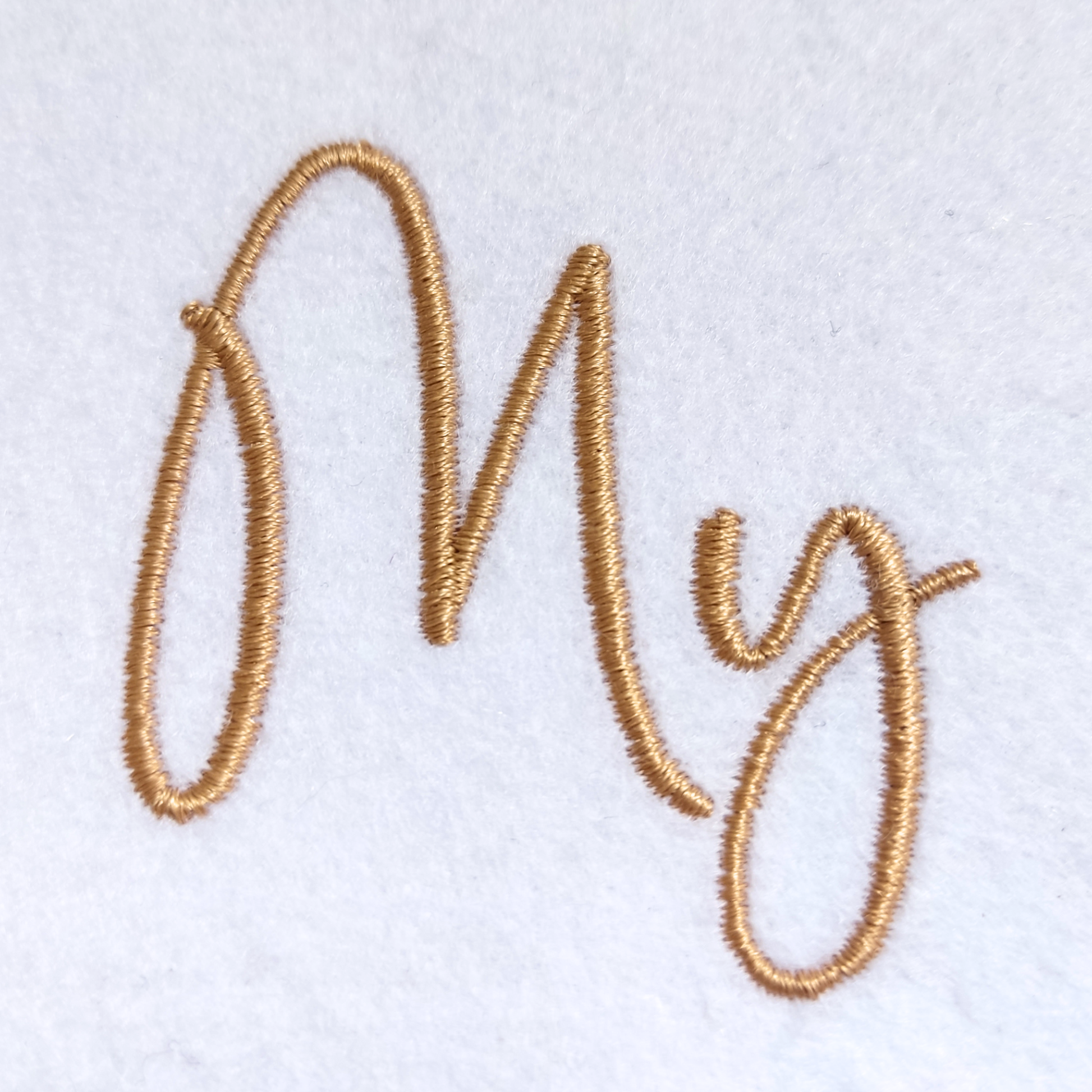 Gold embroidered cursive lettering spelling 'My' on a white textured fabric background.